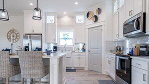 A modern kitchen with white cabinetry, stainless steel appliances, wicker chairs, and a breakfast bar. - Indian Sunrise- peaceful/short stroll to beach! (Galveston)