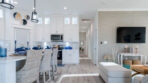 A modern kitchen with white cabinets, a microwave, and a dining area with wicker chairs. - Indian Sunrise- peaceful/short stroll to beach! (Galveston)