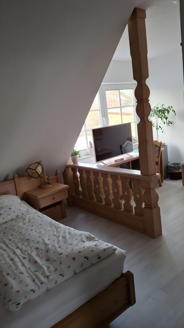 A bedroom with a bed, a desk, a chair, a TV, and a window.