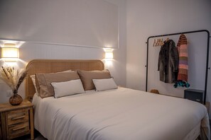 Un lit bien fait, avec une tête de lit en bois, deux tables de chevet avec des lampes et un portant à vêtements avec des vêtements suspendus.