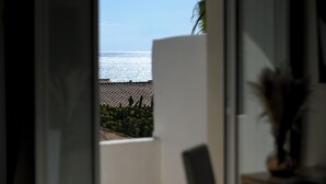 Vista attraverso una porta aperta su un balcone con ringhiera in metallo, affacciato su uno specchio d'acqua.