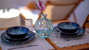 Un tavolo apparecchiato con piatti blu, un vaso di vetro trasparente con fiori rosa e un bicchiere.
