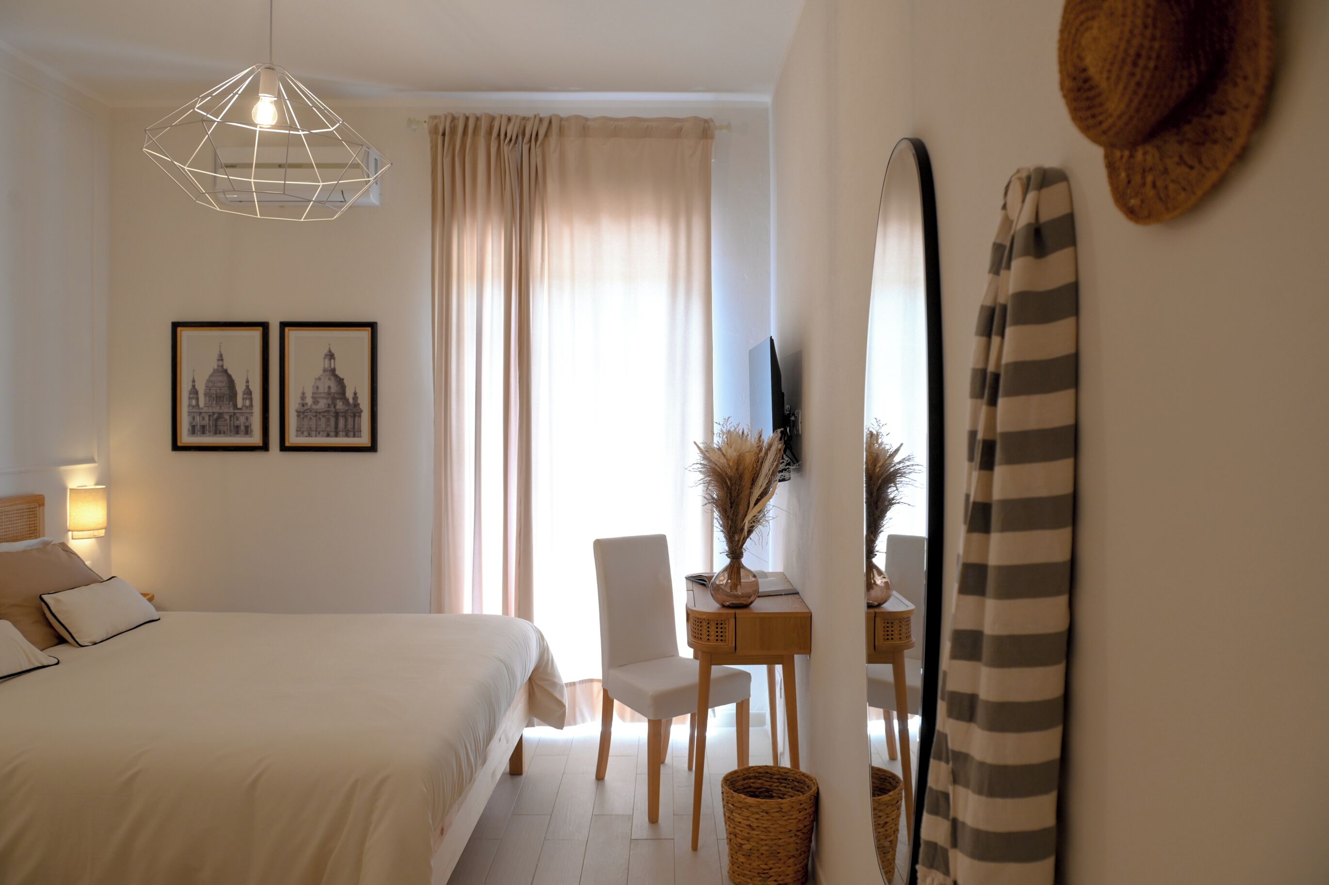 A bedroom with a bed, a desk, a chair, a hanging light fixture, and a mirror.