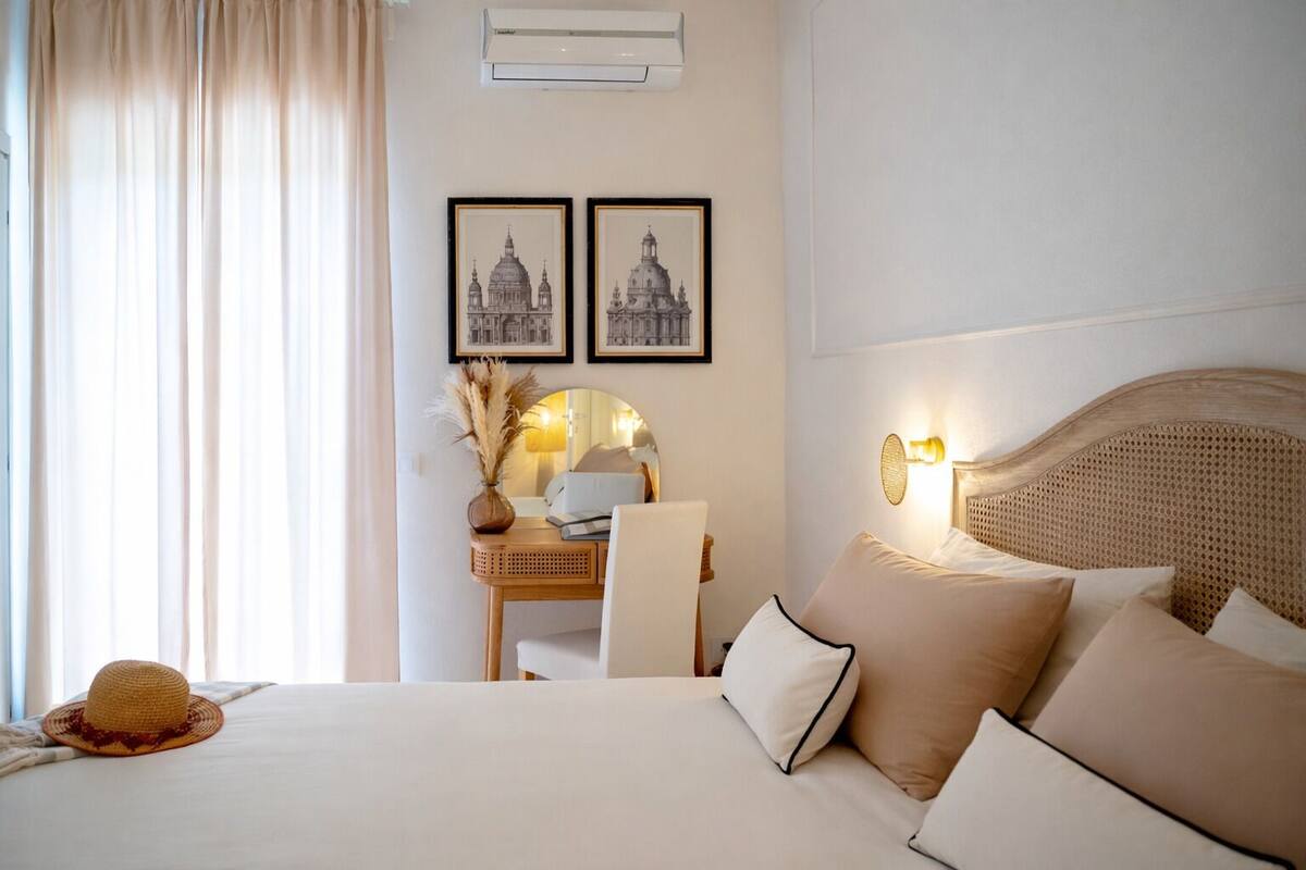 Hotellihuone, jossa on sänky, työpöytä tuolilla, lamppu ja kaksi kehystettyä kuvaa seinällä.