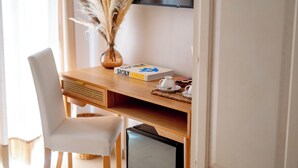 Una scrivania in legno con un portatile, una sedia bianca, un vaso con piante essiccate, un libro e una piccola TV.