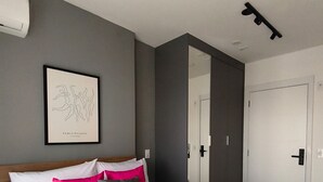 Ein modernes Hotelzimmer mit einem großen Bett, einem gerahmten Kunstwerk an der Wand und einer Tür zu einem weiteren Raum.
