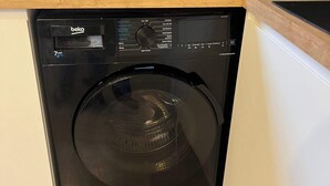 Cozinha compacta e moderna, com máquina de lavar louça preta embutida, cafeteira e chaleira na bancada.