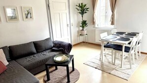 A living room with a sofa, a small table, a dining table with chairs, a potted plant, and a window with curtains. - Cozy vacation apartment in the countryside (Sulzbach-Laufen)
