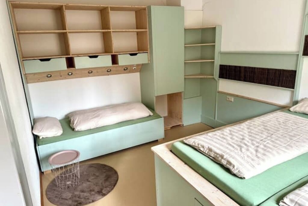 A bedroom with a bed, a built-in wardrobe, a small stool, and a round rug.