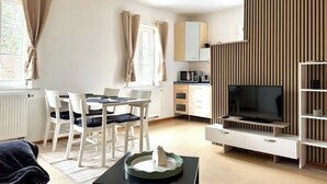 A modern living room with a dining area, a flat-screen TV, and a kitchen area. - Cozy vacation apartment in the countryside (Sulzbach-Laufen)