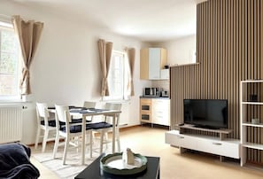 Ein modernes Wohnzimmer mit Essbereich, einem Flachbildfernseher und einer Küchenzeile.