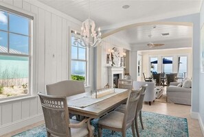 Ein Essbereich mit Holztisch, Korbstühlen, einer Chandelierleuchtre und Blick auf den Strand.