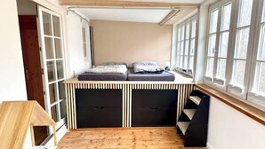 Ett kompakt rum med en loftssäng, inbyggd förvaring och stora fönster.