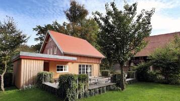 A wooden house with a red roof, surrounded by a well-maintained garden and trees.