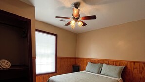 Een slaapkamer met een bed, een plafondventilator, een raam en een houten garderobe.