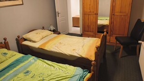 Ein Schlafzimmer mit zwei Einzelbetten, einem Holzschrank, einem Stuhl und einer Tür zu einem anderen Raum.