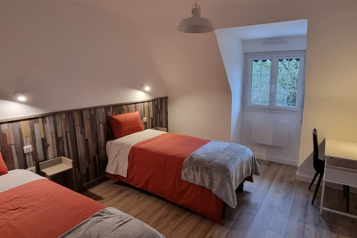 A bedroom with two beds, a desk, and a window.