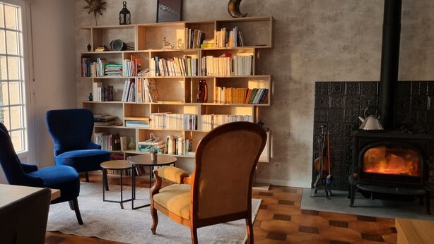 A cozy living room with a fireplace, a bookshelf, and two chairs. - Au Pré du Chêne (Le Faouët)