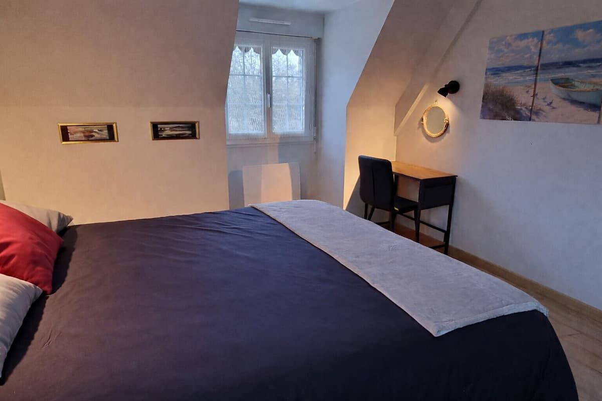A bedroom with a bed, a desk, two chairs, and a window.