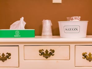 A bathroom vanity with a tissue box labeled 'Spring Grove,' a container labeled 'SAVON,' and decorative metal handles on the drawers.