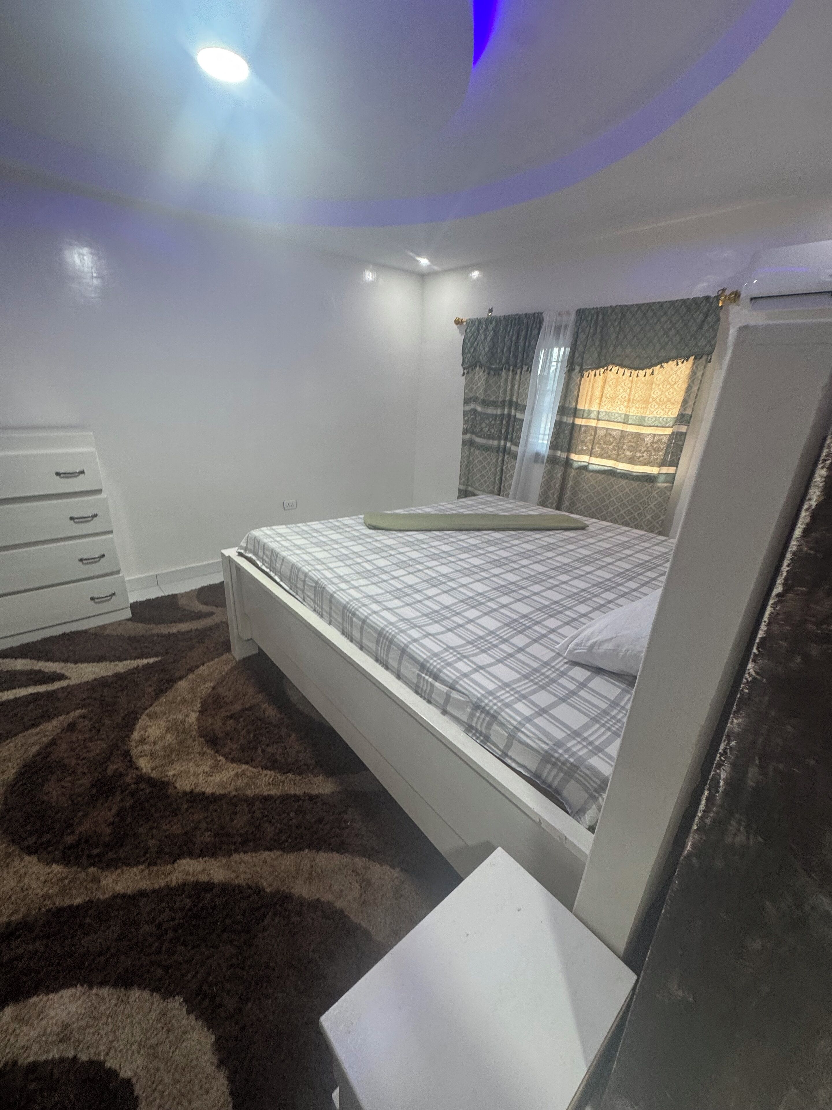 A bedroom with a bed, a dresser, a nightstand, and a ceiling light.