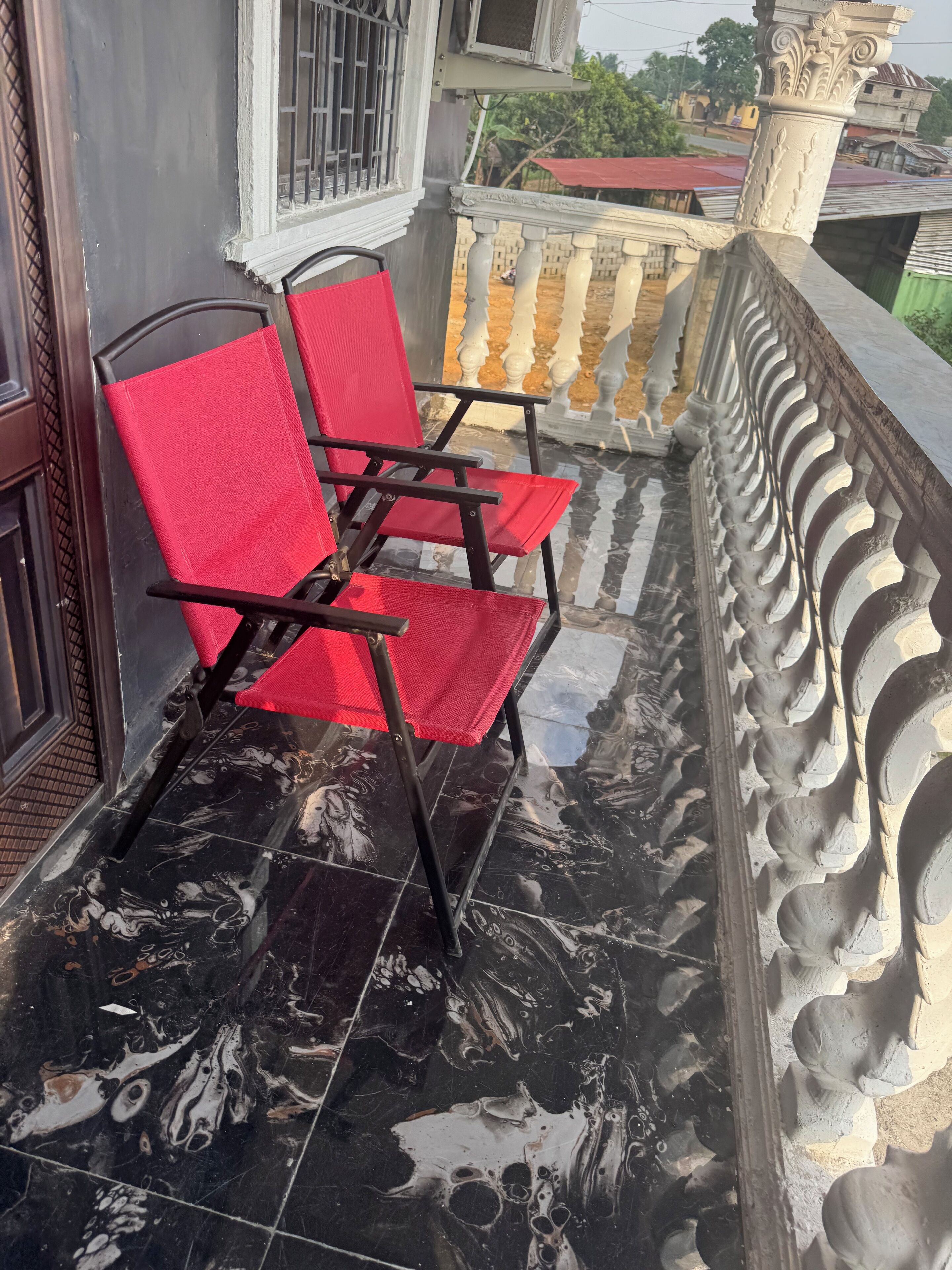 A balcony with two red chairs and a decorative balustrade.