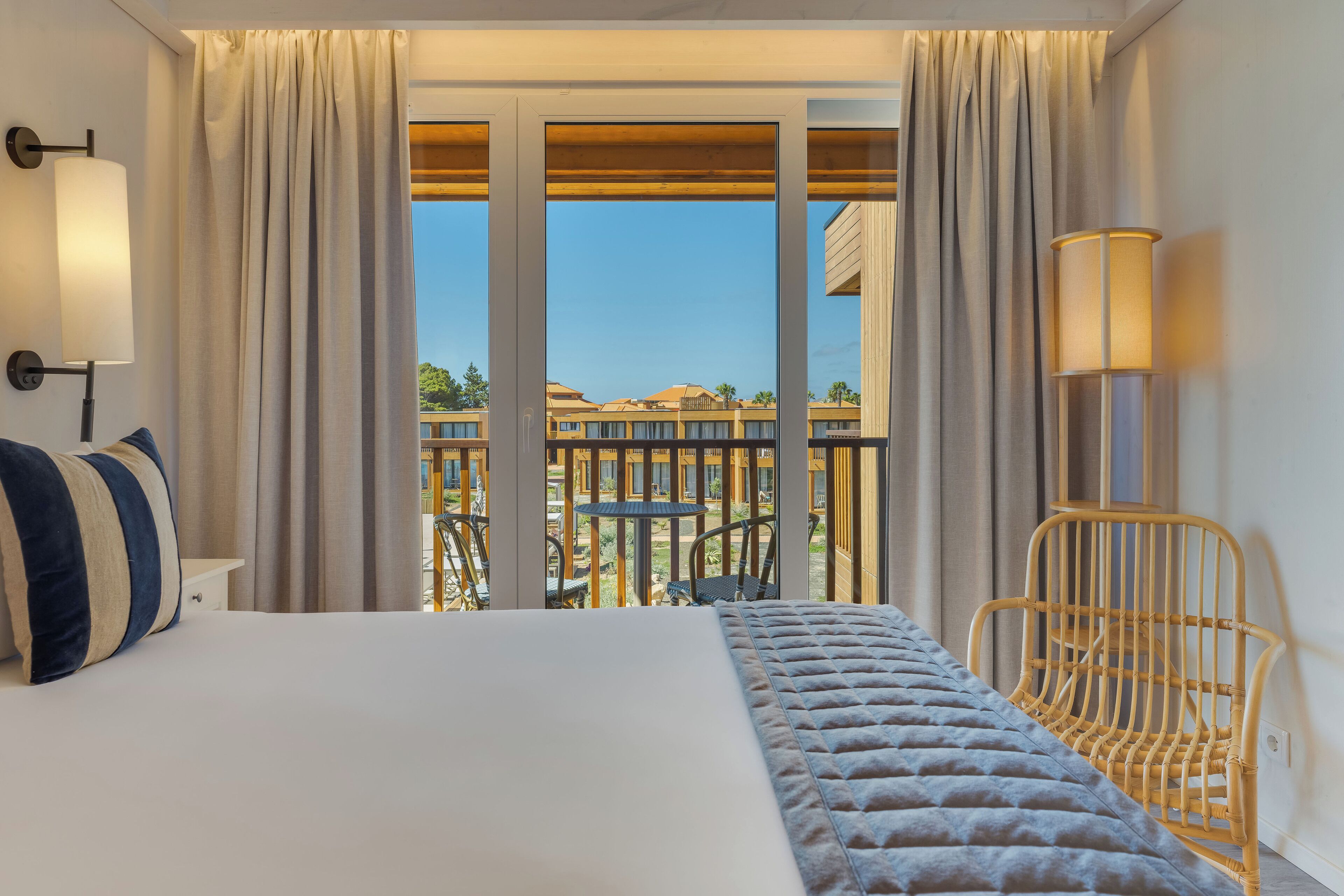 Une chambre d’hôtel avec un lit, des rideaux, une lampe, une chaise et une vue sur l’extérieur.