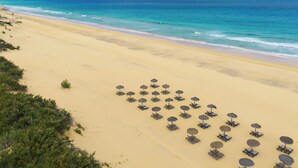 A beach with rows of sun loungers and umbrellas, a clear view of the ocean, and distant mountains. - Pestana Dunas All Inclusive Eco Resort (Porto Santo)