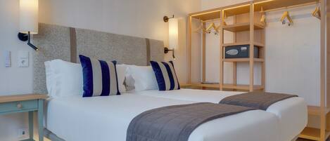 Una cama doble con colcha gris, una mesita de noche de madera, una lámpara de pared y un armario de madera con espacio para colgar.