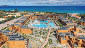 A resort with multiple wooden buildings, a central pool, and a view of the ocean. - Pestana Dunas All Inclusive Eco Resort (Porto Santo)