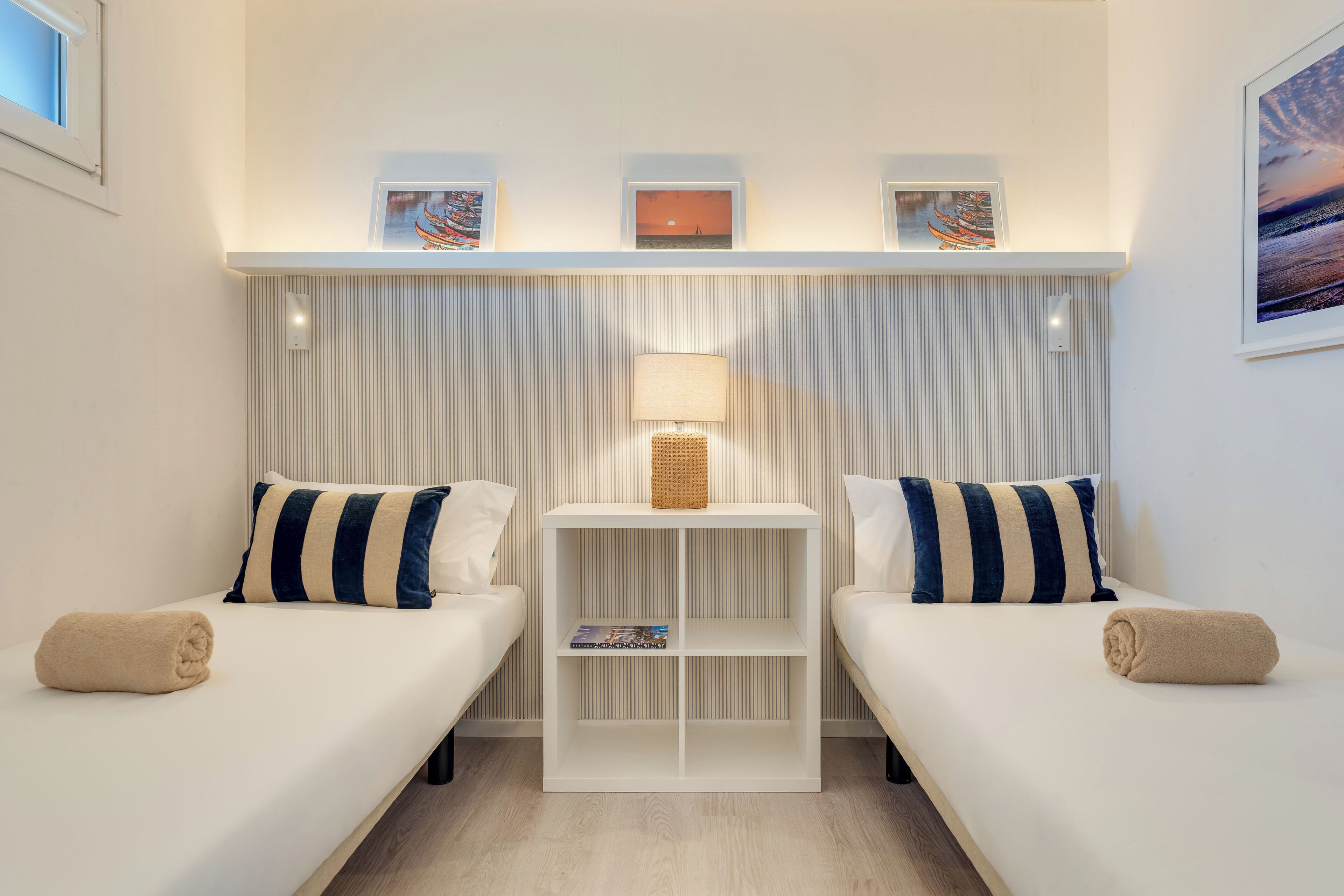 Une chambre d’hôtel avec deux lits, une table de chevet avec une lampe et des tableaux encadrés au mur.