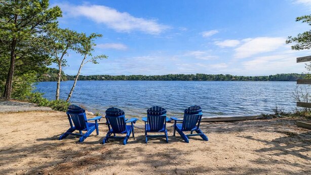 Drie blauwe Adirondack-stoelen kijken uit over een meer met een heldere lucht.