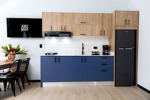 Una cocina moderna con armarios superiores de madera, un mueble bajo azul, un refrigerador negro y un televisor de pantalla plana en la pared.