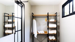 Un baño moderno y compacto con un espejo grande en la pared, un armario de madera empotrado para toallas y una ventana que deja entrar luz natural.