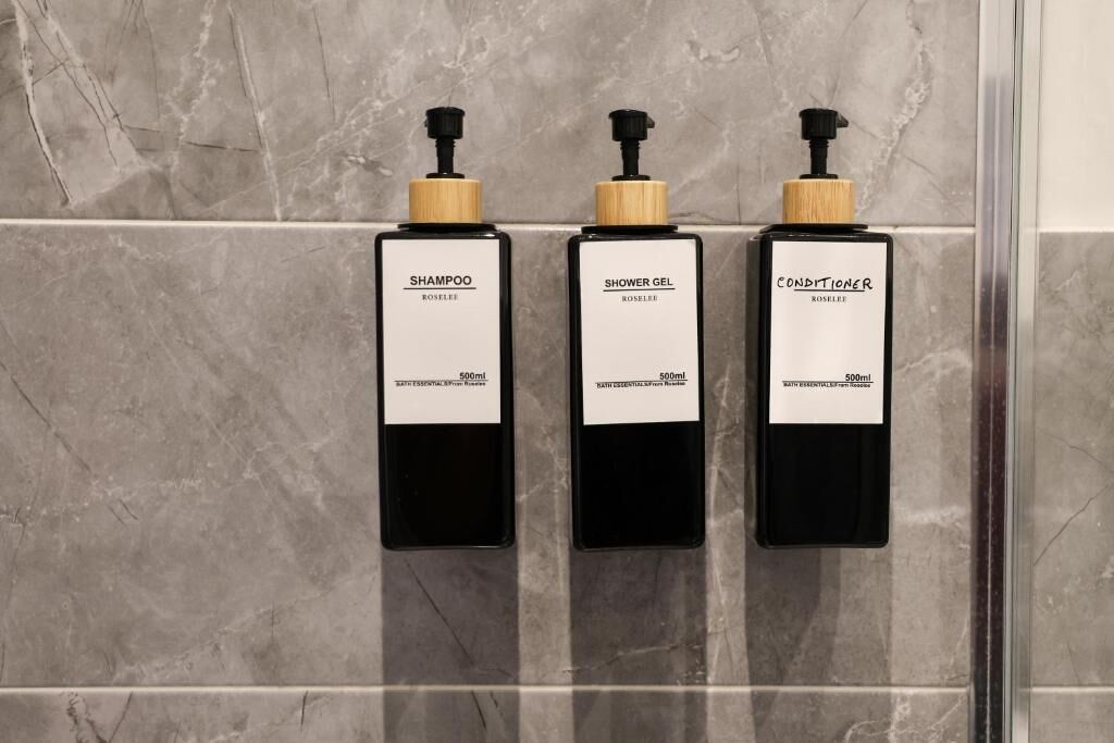 Three black bottles with wooden pumps on a tiled wall.