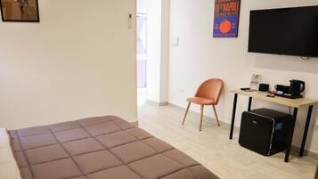 A room with a bed, a desk with a chair, a television, and a small black cabinet.
