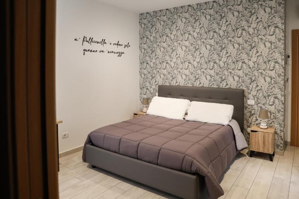 Un dormitorio con cama, mesita de noche, pared con estampado floral y una puerta.