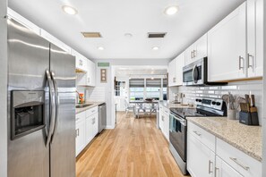 A modern kitchen with stainless steel appliances, white cabinetry, and a wooden floor. - Walk to Beach | Dog-Friendly | Reel Paradise (Ormond Beach)