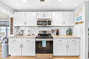 A modern kitchen with white cabinetry, stainless steel appliances, and a granite countertop. - Walk to Beach | Dog-Friendly | Reel Paradise (Ormond Beach)