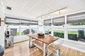 Ein Zimmer mit Holztisch, einer Bank und großen Fenstern mit Jalousien.