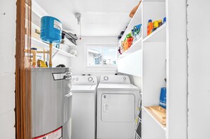 Ein Waschraum mit zwei Waschmaschinen, einem blauen Boiler und Regalen mit Reinigungsmitteln.