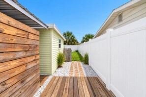 Eine Holzterrasse führt zu einem Haus mit weißem Zaun und grüner Außenverkleidung.