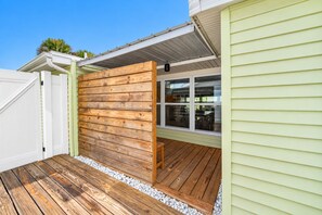 A wooden deck with a white fence, a window with a view of the interior, and a light-colored exterior wall. - Walk to Beach | Dog-Friendly | Reel Paradise (Ormond Beach)