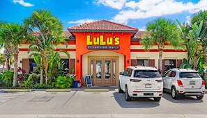 Ein Restaurant namens 'Lulu's Oceanside Grill' mit roter und orangefarbener Fassade, zwei geparkten Geländewagen und tropischen Pflanzen.