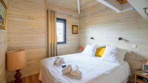 Un dormitorio con paneles de madera, una cama, una mesita de noche, una lámpara y una ventana con cortinas.