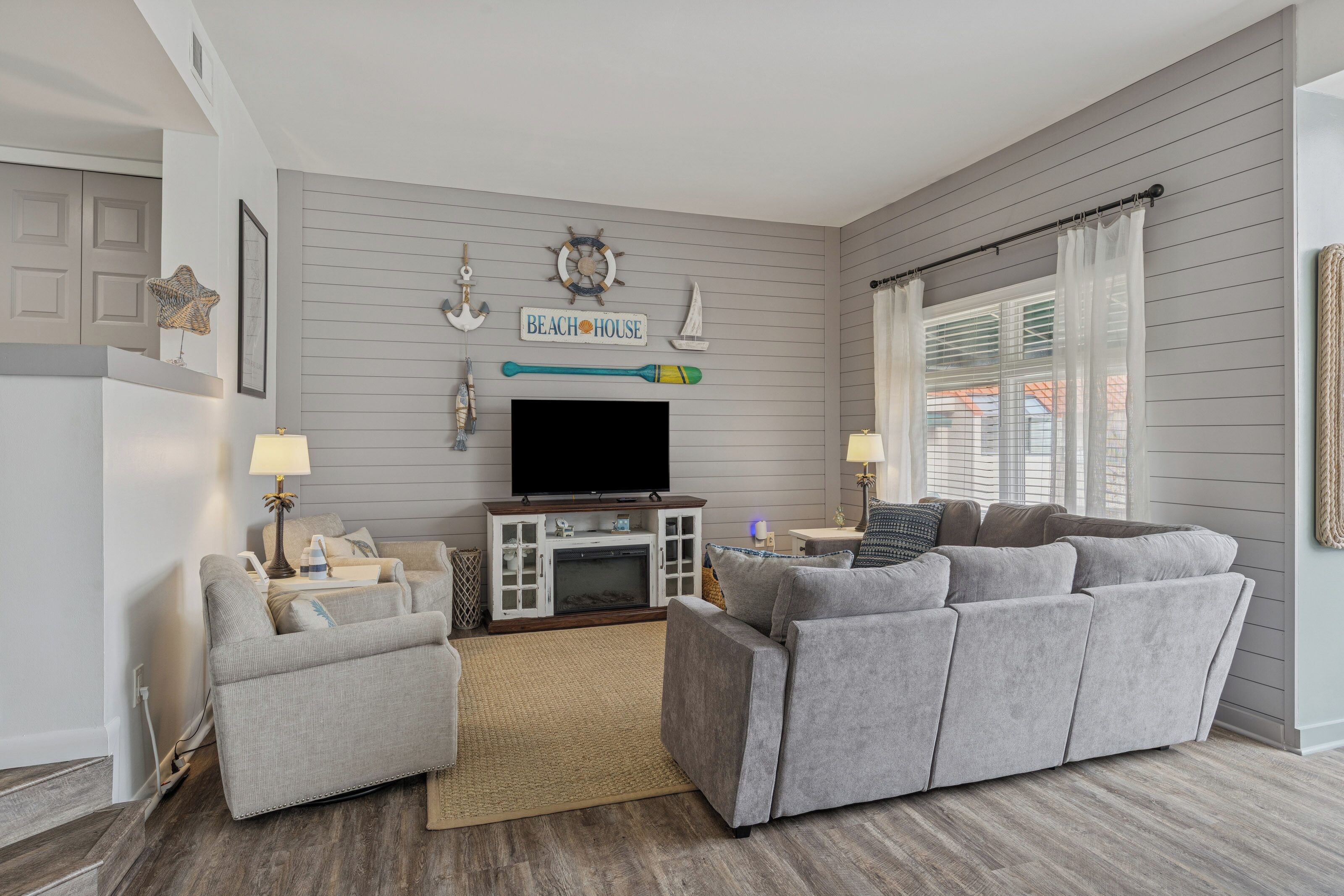 A living room with a gray sofa, a television, and nautical-themed wall decor.