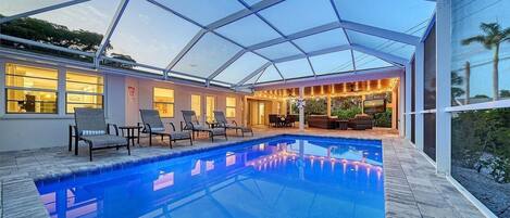 A covered swimming pool with lounge chairs and a dining area.