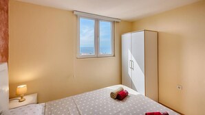 A bedroom with a bed, a nightstand, a wardrobe, and a window with a view. - Apartman ZIS 5L (Opština Bar)