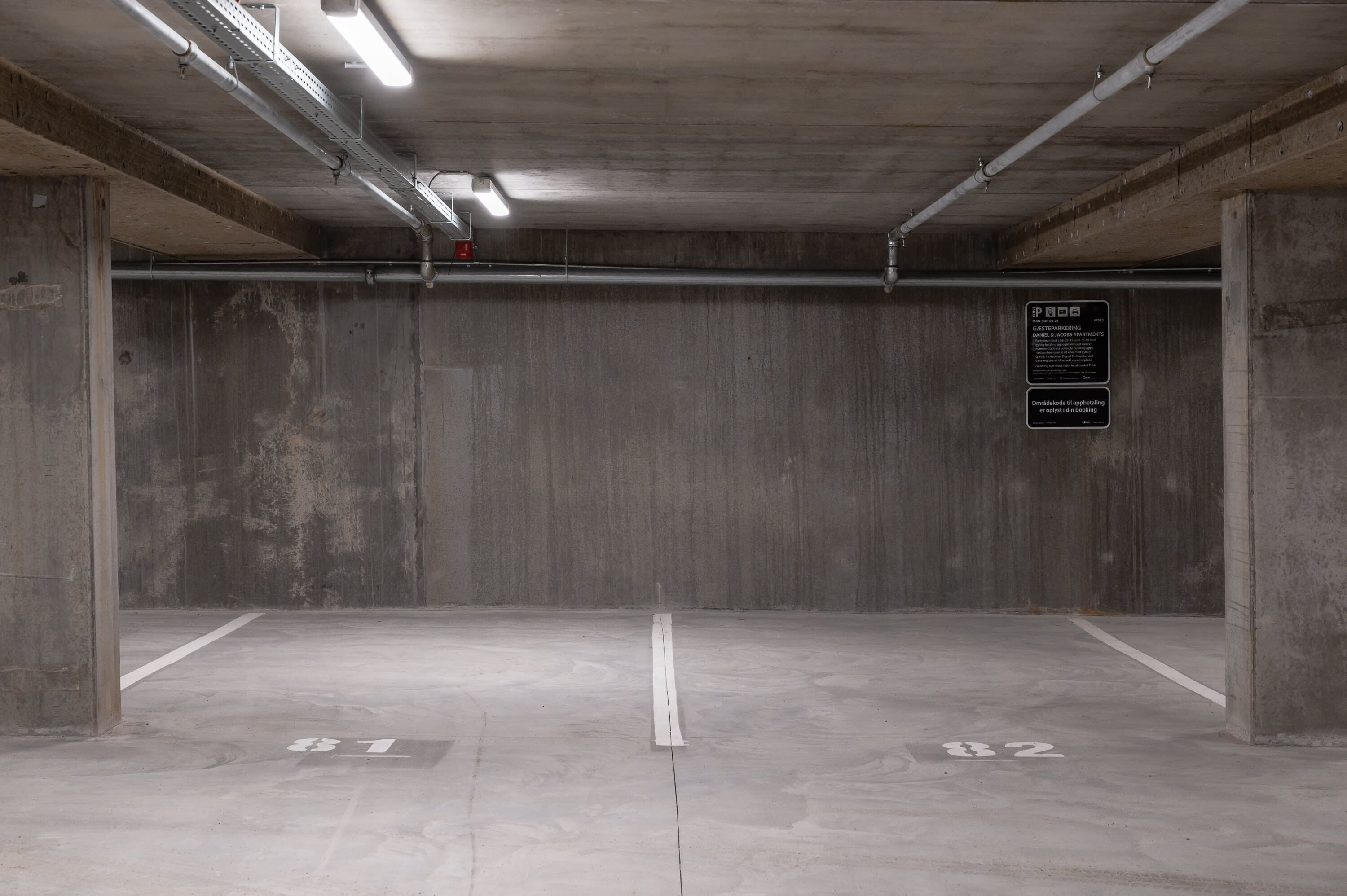 Een lege parkeergarage met betonnen wanden en vloeren, gemarkeerde parkeerplaatsen en bovenop tl-verlichting.