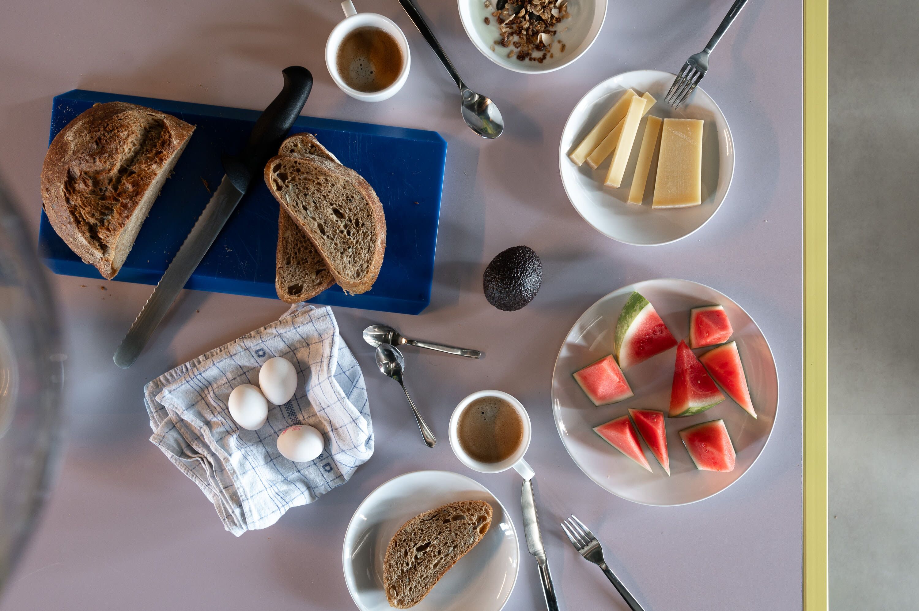A breakfast setting with bread, eggs, coffee, and watermelon slices on a table.